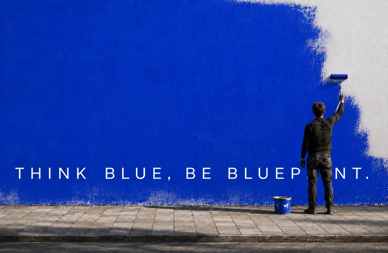 Pintor cobrindo uma parede com tinta azul sobre a frase Think Blue, Be Blueprint